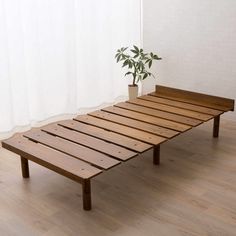 a wooden bed frame sitting on top of a hard wood floor next to a potted plant