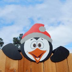 a penguin with a santa hat on top of a wooden fence