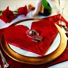 a table setting with red napkins, silverware and gold place settings on it