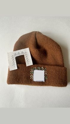 a brown beanie hat with a white photo frame on it and a card attached to the front