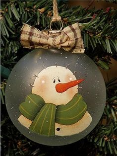 a glass ornament with a snowman on it hanging from a christmas tree