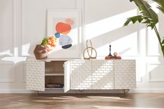 a white sideboard with plants on it in front of a painting and potted plant