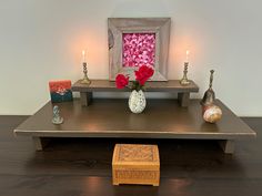 a wooden table topped with two vases filled with flowers and candles next to a painting