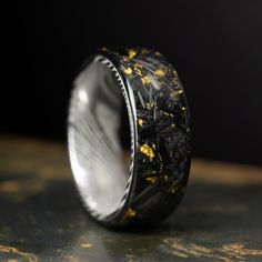 a black and gold wedding band with an intricate design on it's side, sitting on top of a table