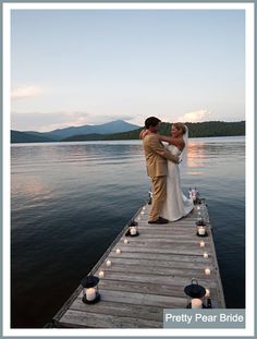 a bride and groom standing on a dock with candles in front of the water at sunset