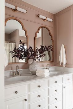 a bathroom with pink walls and two mirrors on the wall, white cabinets and drawers