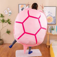 a woman in a pink turtle costume standing on a white mat with her arms outstretched