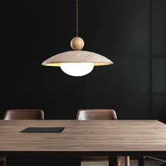 a wooden table with chairs and a light hanging from it's center point in a dark room