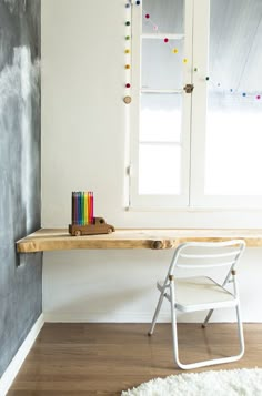 a white chair sitting under a window next to a wooden table with colored pencils on it