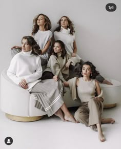 four women are sitting on a round white bench and posing for the camera with their arms around each other