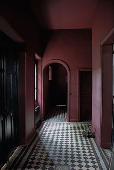 an empty hallway with black and white checkered flooring, red walls and doors