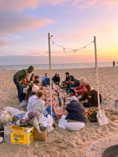 a group of people sitting on top of a sandy beach next to the ocean at sunset