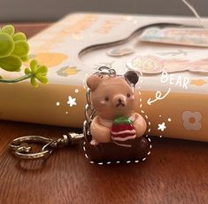 a bear keychain sitting on top of a wooden table next to a book