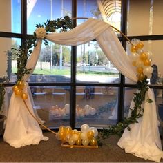 an arch decorated with balloons and greenery in front of a window at a wedding