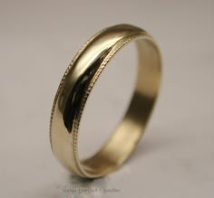 a gold wedding ring with engraved details on the outside and inside, sitting on a white surface