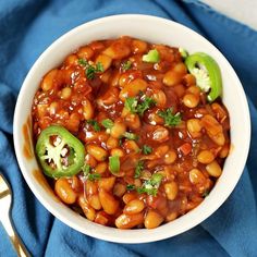 a white bowl filled with beans and broccoli on top of a blue cloth