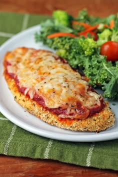 a white plate topped with meat covered in cheese and veggies next to a salad