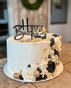 a white cake with black and gold decorations on it that says happy birthday written on top