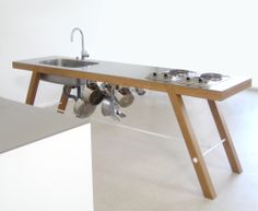 a kitchen table with pots and pans hanging from it's legs, in front of a white wall