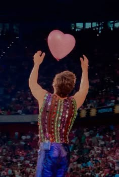 a man holding a heart shaped balloon while standing on top of a basketball court in front of a crowd