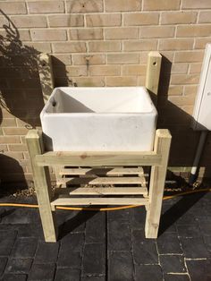 a white sink sitting on top of a wooden stand next to a brick wall in front of a building