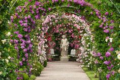 a statue in the middle of a garden filled with pink and white flowers, surrounded by greenery