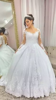 a woman in a white wedding dress looking at herself in the mirror with her hands on her hips