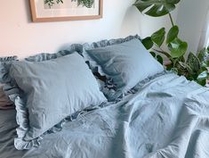 a bed with blue sheets and pillows in a room next to a potted plant