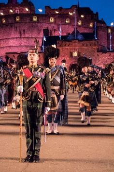 a group of men in kilts standing next to each other on a street near a castle