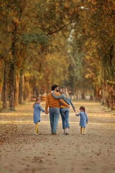 a family walking down a dirt road in the fall with leaves on the ground and trees lining both sides