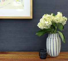 a white and blue vase with flowers in it on a wooden table next to a painting