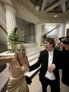 two people dressed up in formal wear walking down the stairs with masks on their faces