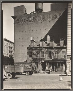 an old black and white photo of cars parked in front of a tall building with two chimneys