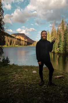 a man standing in front of a body of water with trees and mountains in the background