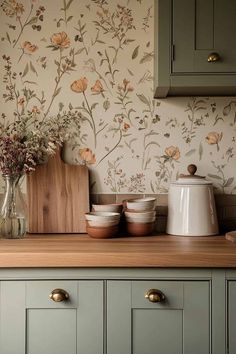 a kitchen counter with flowers on the wall and wooden cutting board in front of it