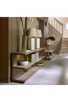 there is a shelf with books and vases on it next to the stair case