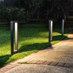 three metal poles on the side of a sidewalk in front of some green grass and trees