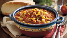 a bowl filled with corn and meat soup next to slices of bread on a table