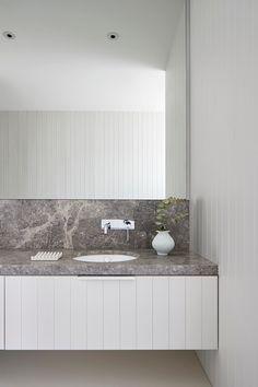 a bathroom with marble counter tops and white cabinets, along with a vase filled with flowers