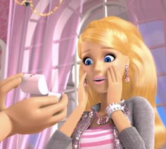 a barbie doll holding a nintendo wii game controller next to a blonde haired woman with blue eyes