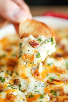 a close up of a person dipping some food into a bowl with broccoli and cheese on it