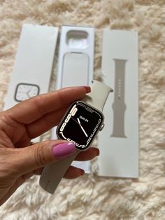 a hand holding an apple watch in front of a box with the case open and it's strap undone