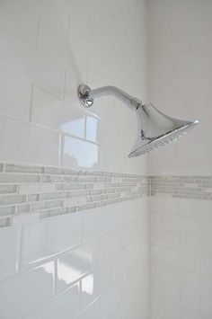 a shower head in the corner of a white tiled bathroom with gray grouting