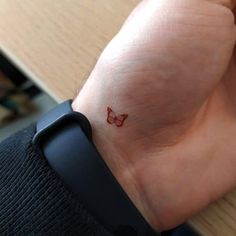 a small red butterfly tattoo on the wrist