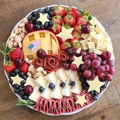 a platter filled with cheese, grapes, strawberries and other fruit on top of a wooden table