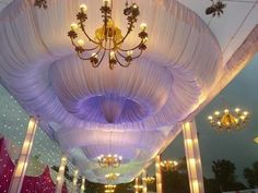 the ceiling is decorated with white drapes and chandeliers for an elegant wedding