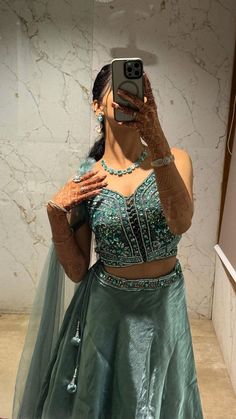 a woman taking a selfie in front of a mirror wearing a green skirt and crop top