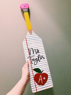 a person holding up a piece of paper with an apple on it and a pencil sticking out of it