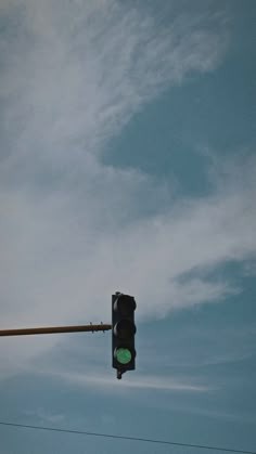 a traffic light hanging from the side of a metal pole under a cloudy blue sky