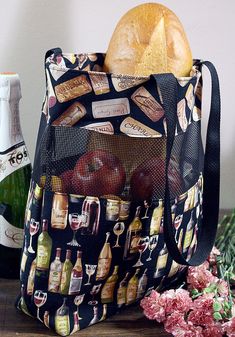 a bag full of bread and wine bottles on a table next to flowers with pink carnations in the background